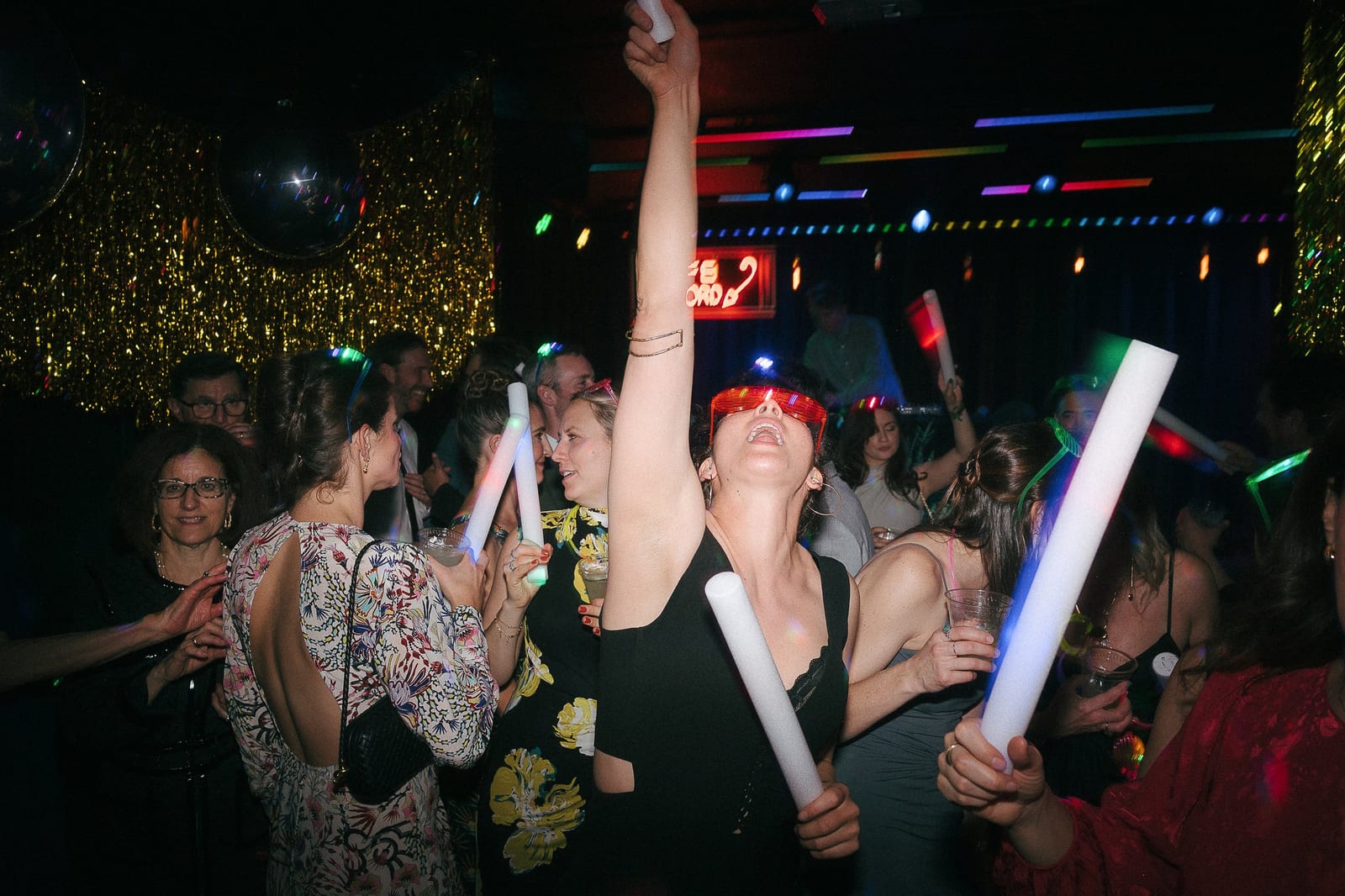 Guests dancing with glow sticks under disco balls and gold streamers