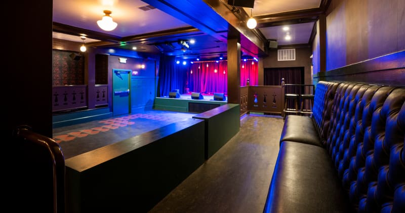 A tufted leather booth in the foreground, with the stage lit red and pink beyond